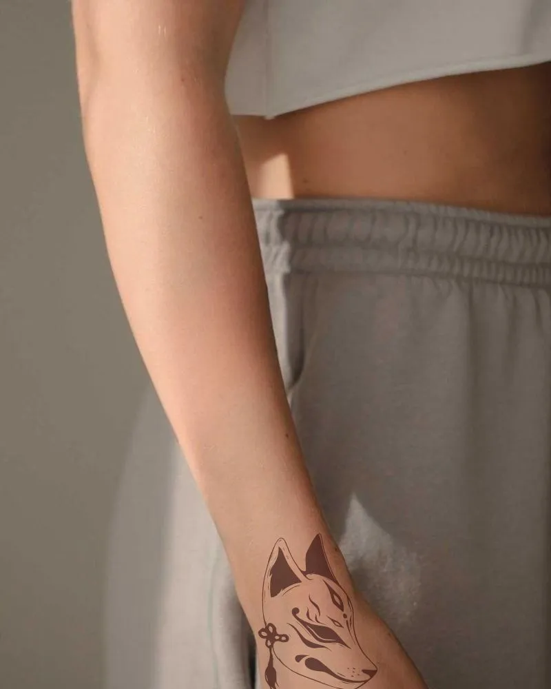 A half-body photograph of a woman with a kitsune fox tattoo on her hand.